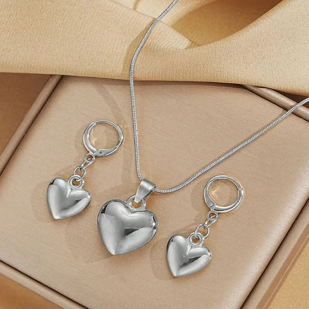 gold plated heart dangle earrings necklace set with glossy love heart pendant and matching dangle earrings on beige fabric